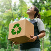 Persona sosteniendo caja de cartón con símbolo de reciclaje y botellas plásticas
