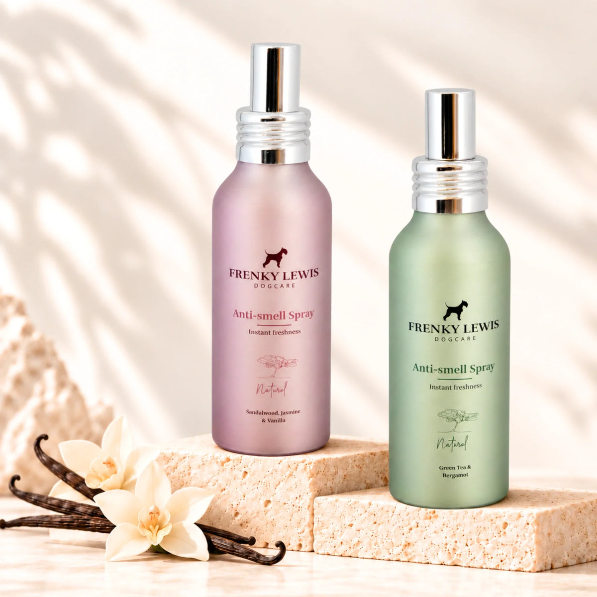 Dos sprays neutralizadores de olores para perros Frenky Lewis, en botellas rosa y verde, sobre soportes de piedra clara, con vainilla y decoración vegetal en un entorno luminoso.