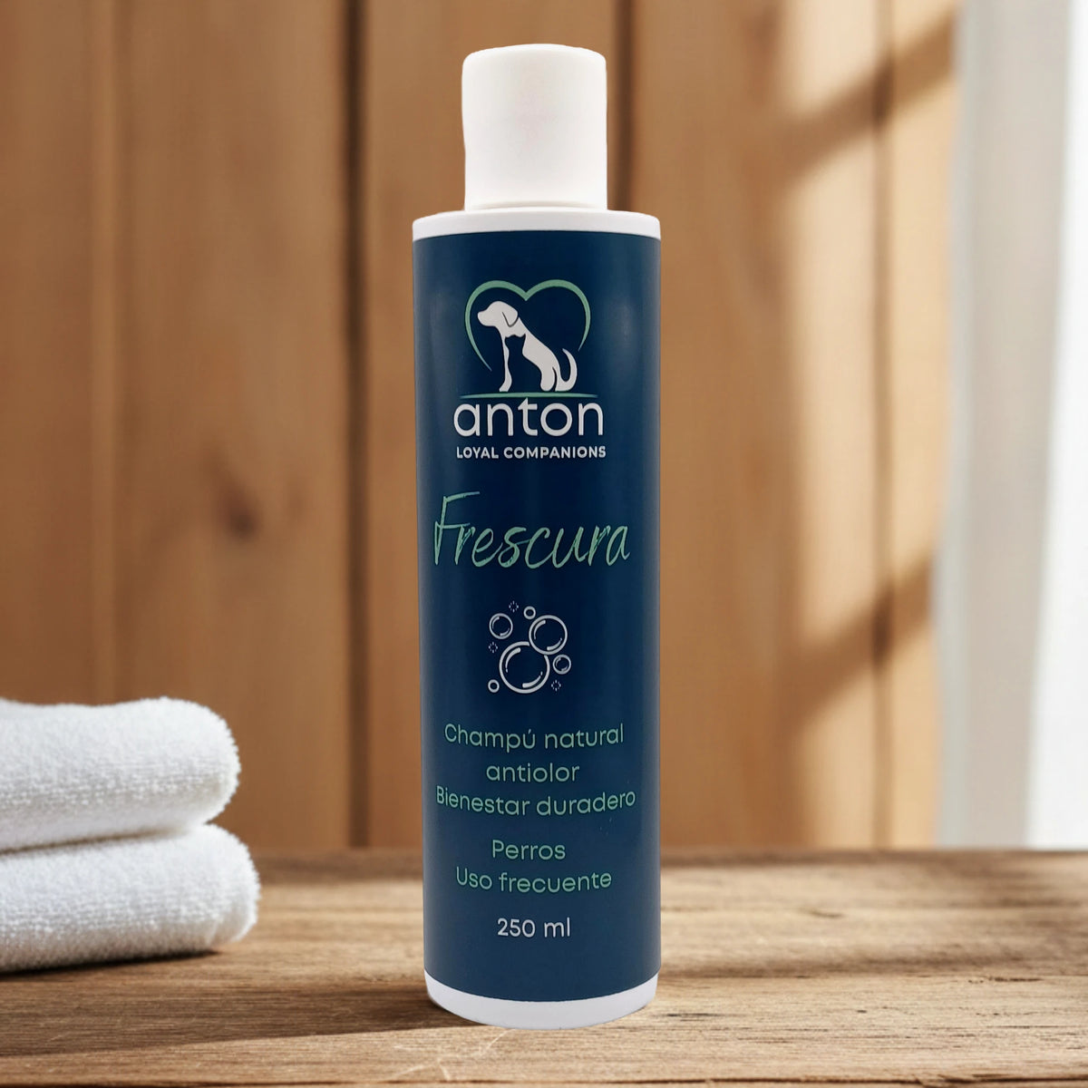 Champú natural Frescura ANTON Loyal Companions para perros, efecto antiólor y bienestar duradero, uso frecuente, frasco de 250 ml sobre mesa de madera con toallas blancas