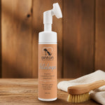 Espuma limpiadora para patas de perros y gatos ANTON LC con cepillo de silicona integrado, presentada sobre una superficie de madera en un entorno cálido y natural.