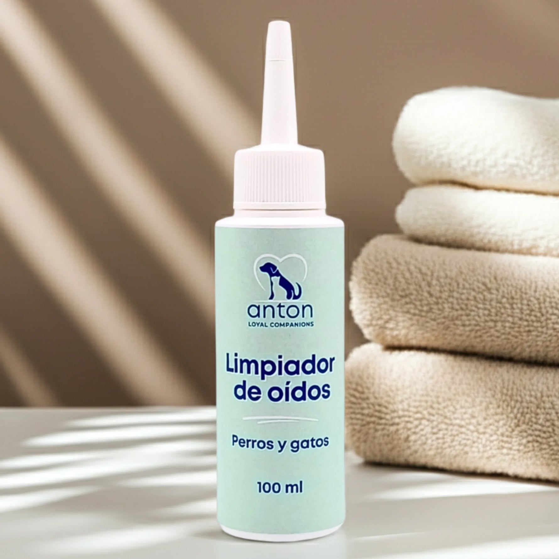 Envase del limpiador de oídos para perros y gatos ANTON sobre fondo beige con toallas suaves.